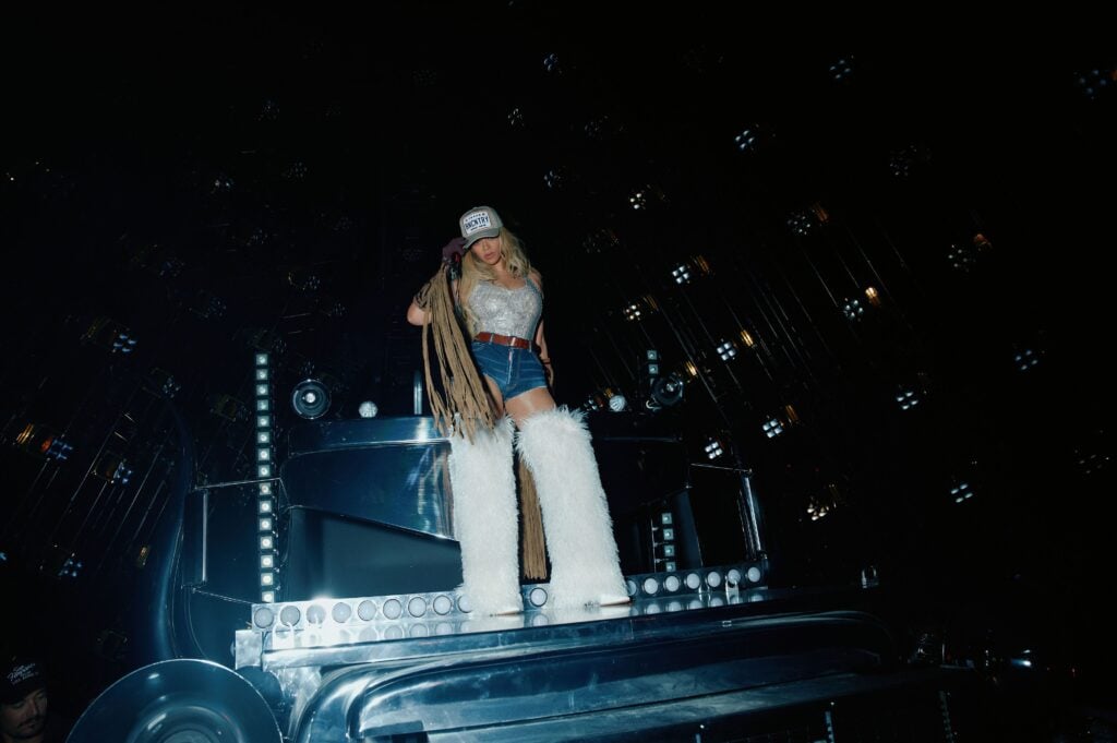 Beyoncé prend la pose en backstage dans des bottes blanches Gedebe, un short en jean et un top à paillettes.